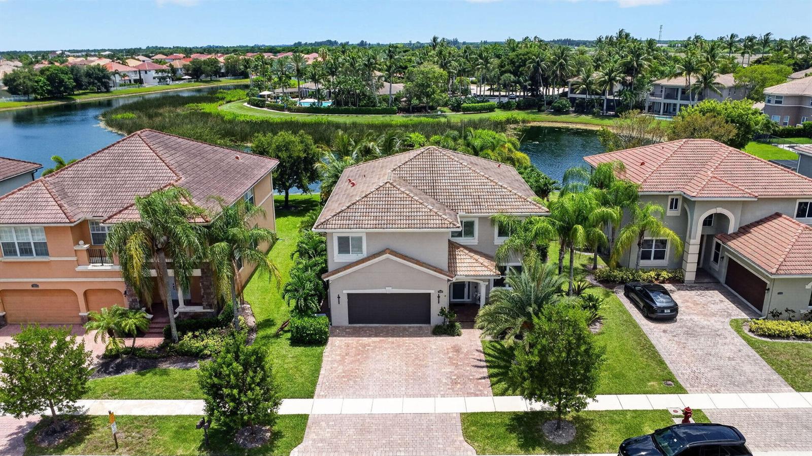 An aerial view shows three suburban houses with tiled roofs situated along a lake — 8890 Cobblestone Point Circle, Boynton Beach FL 33472, BOYNTON BEACH, FL