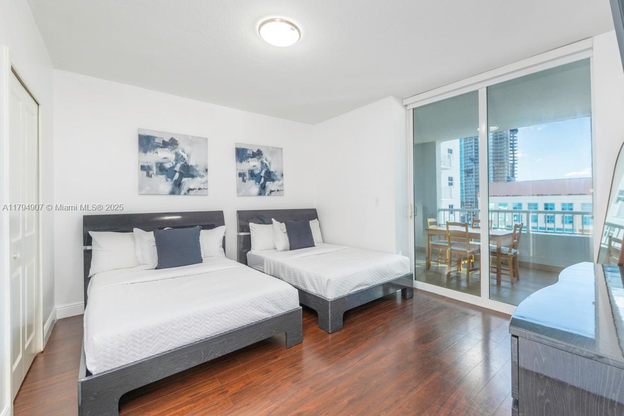 A bedroom features two beds, dark wood flooring, and a sliding glass door to a balcony — 170 SE 14th St # 1905, Miami FL 33131, MIAMI, FL