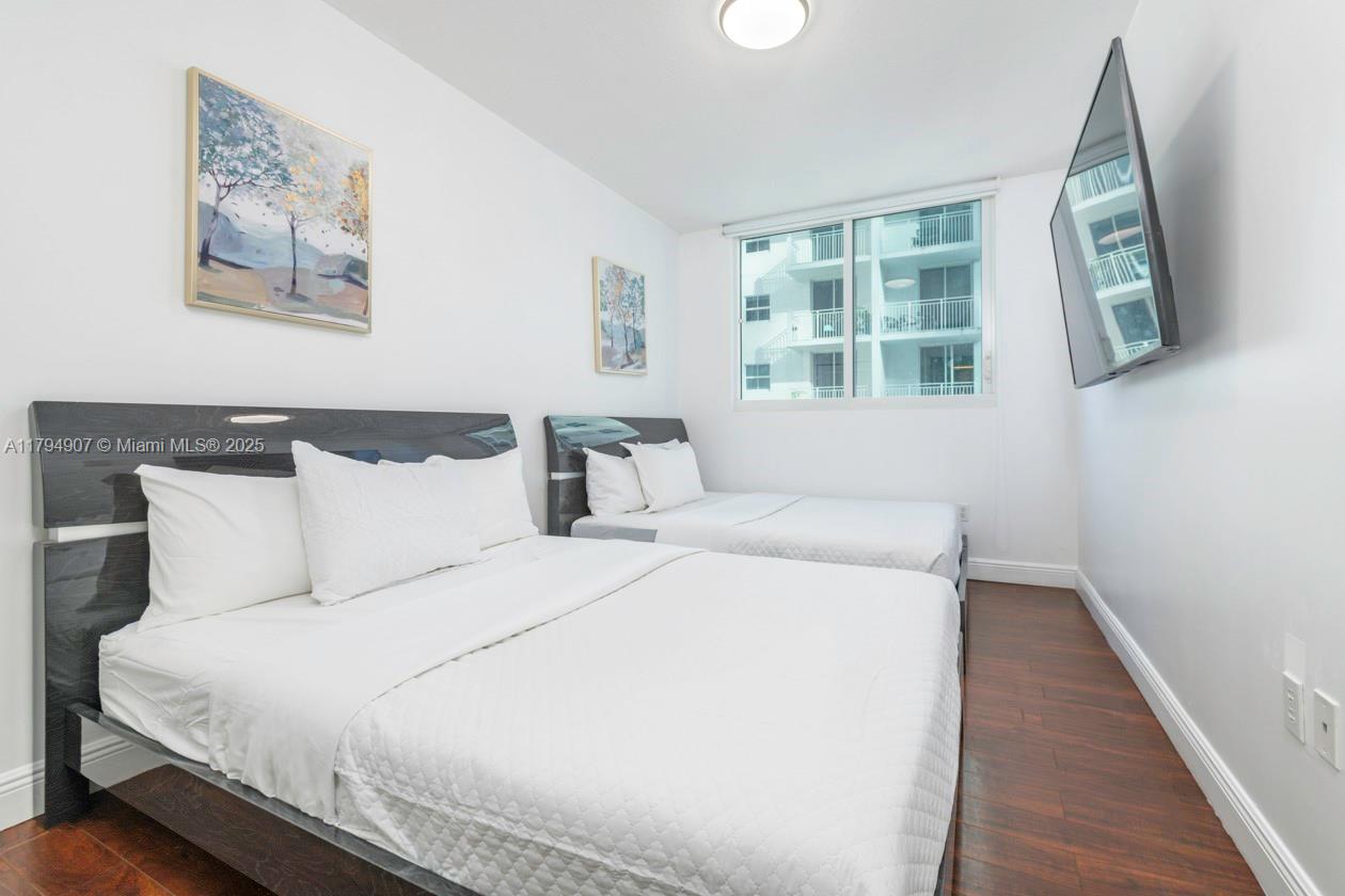 A bedroom features two beds with dark headboards, white bedding, and wood-look flooring — 170 SE 14th St # 1905, Miami FL 33131, MIAMI, FL