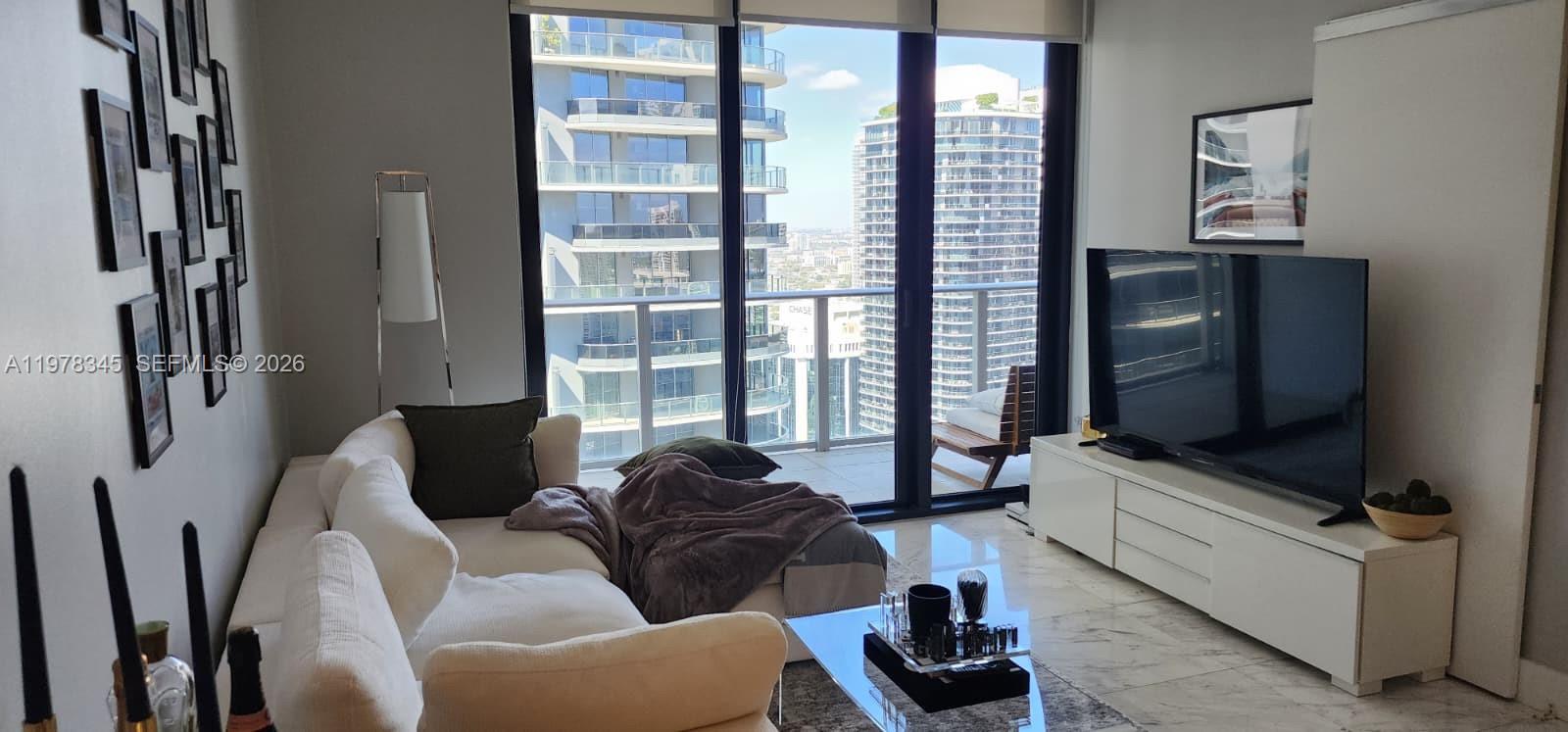 A modern living room features a white sofa, glass coffee table, and floor-to-ceiling balcony windows — 1010 Brickell Ave # 4208, Miami FL 33131, MIAMI, FL