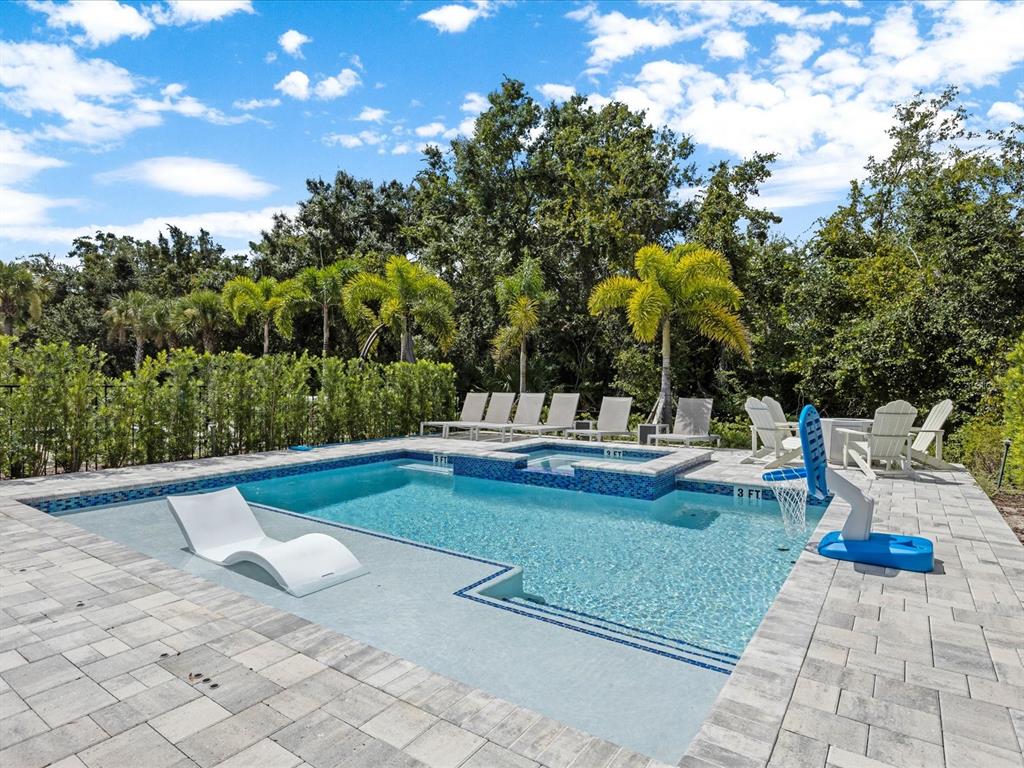 A swimming pool with a sun shelf, spa, and basketball hoop sits on a stone patio — 832 DESERT MOUNTAIN COURT, REUNION, FL