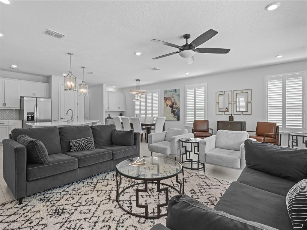 A modern open-concept living room features two dark sofas, a glass coffee table, and kitchen — 832 DESERT MOUNTAIN COURT, REUNION, FL