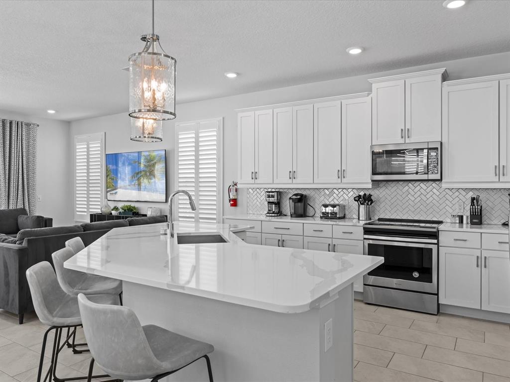 A modern kitchen features white cabinetry, a quartz-topped island, and a herringbone-patterned tile backsplash — 832 DESERT MOUNTAIN COURT, REUNION, FL