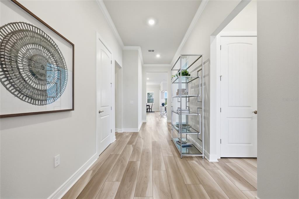 A bright hallway features light wood-look flooring, white doors, and a tall metal display shelf — 15031 CANOPY COVER DRIVE, WINTER GARDEN, FL