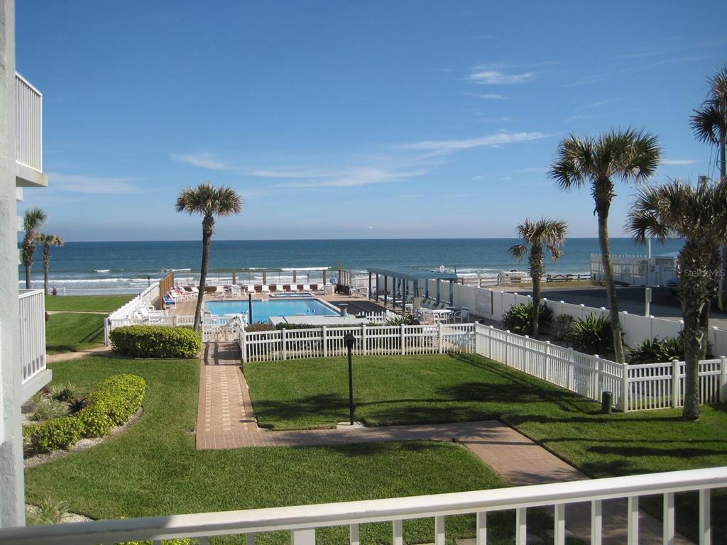 An elevated view of a beachside swimming pool, lawn, and ocean under a clear sky — 1571 S ATLANTIC AVENUE UNIT 203, NEW SMYRNA BEACH, FL