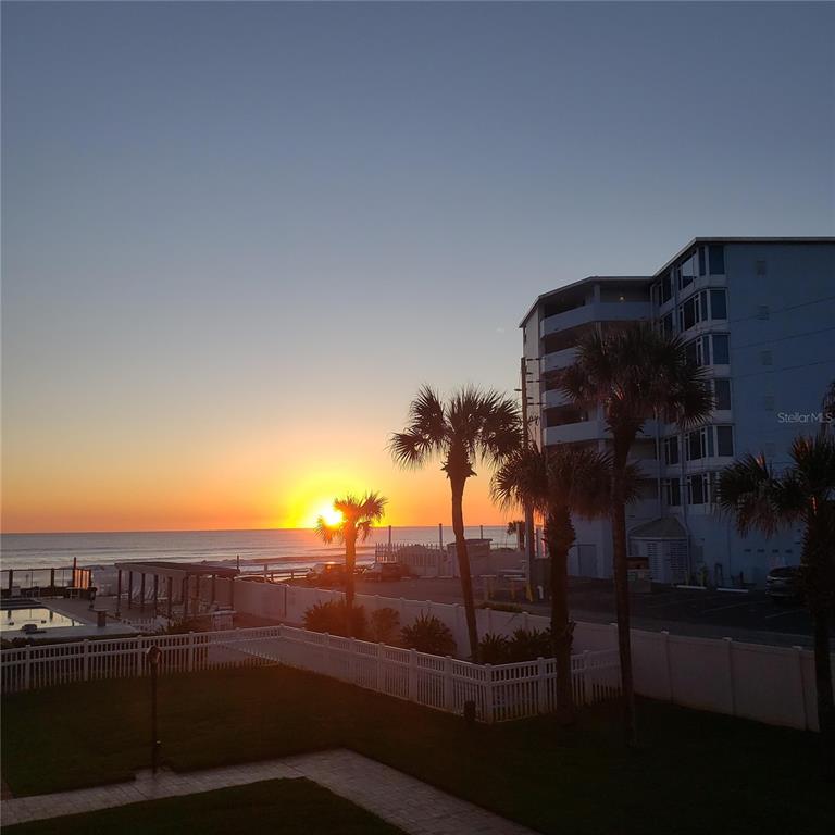 A sunrise view over the ocean with palm trees and a multi-story building nearby — 1571 S ATLANTIC AVENUE UNIT 203, NEW SMYRNA BEACH, FL