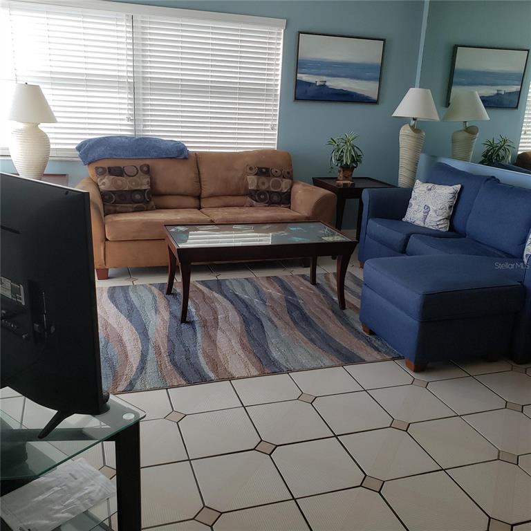 A living room features a brown sofa, a blue sofa with ottoman, and tile flooring — 1571 S ATLANTIC AVENUE UNIT 203, NEW SMYRNA BEACH, FL