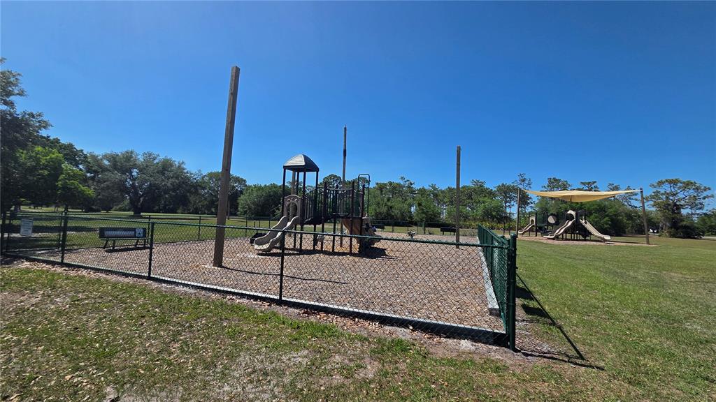 A fenced playground with slides and play structures sits on a grassy lot — GAILLARDIA DRIVE, INDIAN LAKE ESTATES, FL