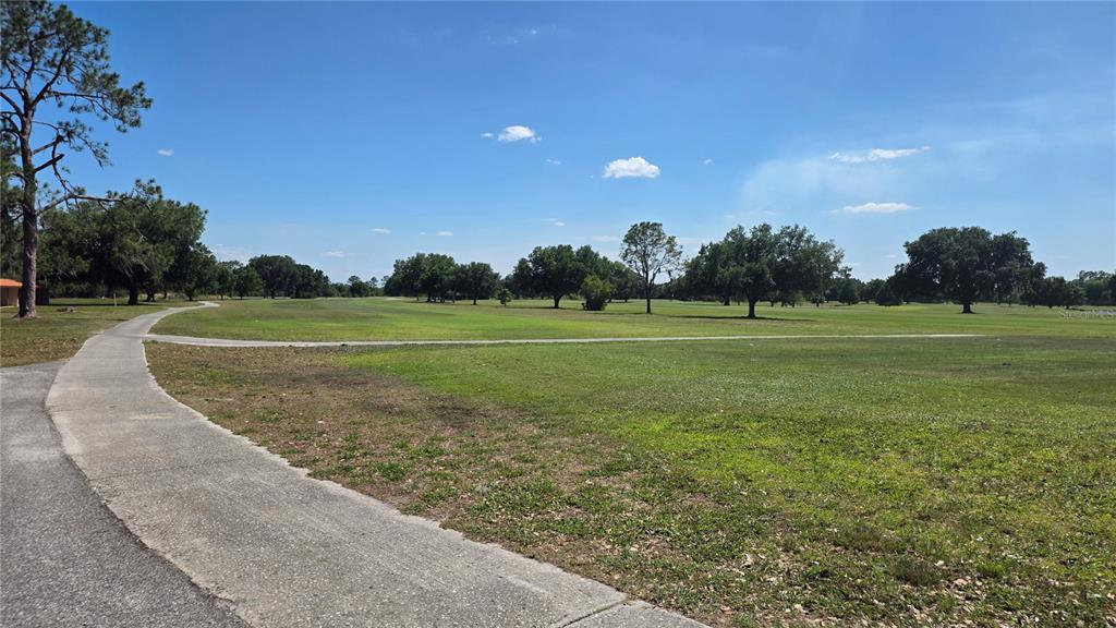 A paved golf cart path winds through a large, grassy field dotted with mature trees — GAILLARDIA DRIVE, INDIAN LAKE ESTATES, FL