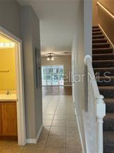 A hallway with tile flooring leads toward a living area with a ceiling fan — 1705 RETREAT CIRCLE, CLERMONT, FL