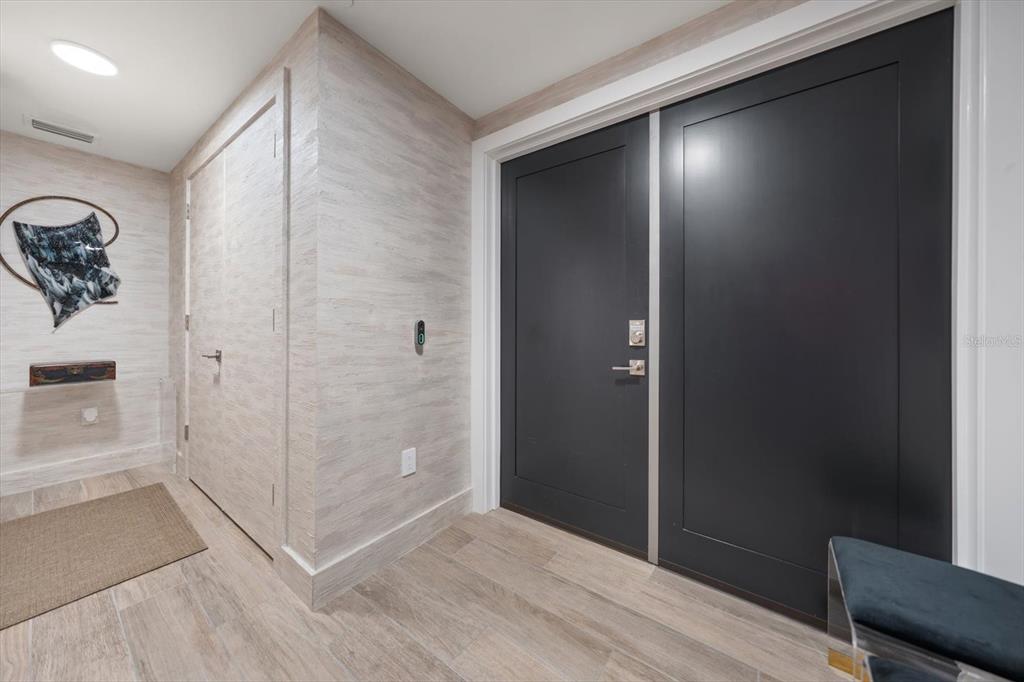 A modern entryway features light wood-look flooring, textured wallpaper, and a double black door — 19816 GULF BOULEVARD UNIT 501, INDIAN SHORES, FL