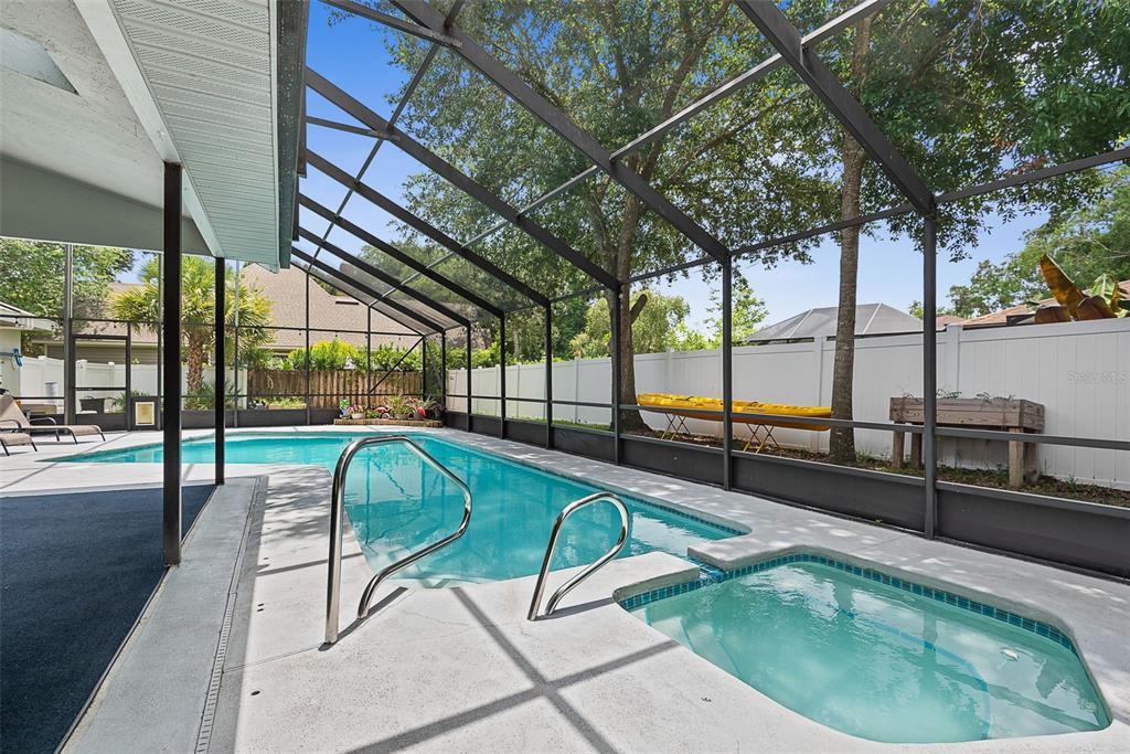 A screened-in pool area with a hot tub, concrete deck, and white privacy fence — 3 ECHO WOODS WAY, ORMOND BEACH, FL