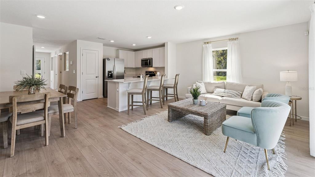 An open-concept living room and kitchen feature light wood floors, white cabinetry, and neutral furniture — 725 PRESTON COVE DRIVE, ST CLOUD, FL