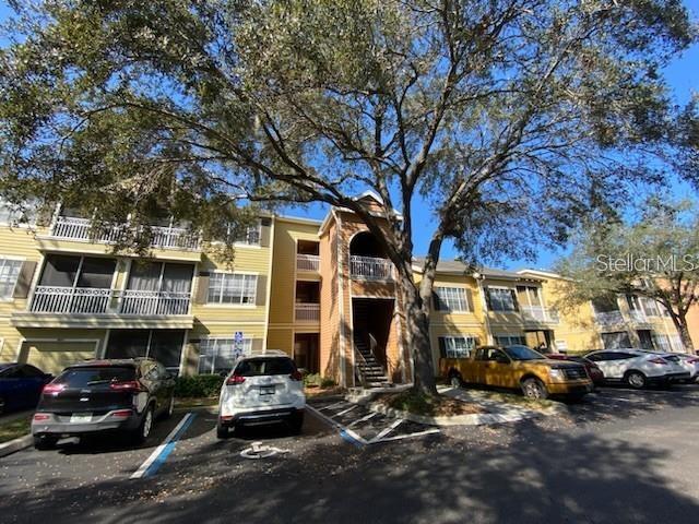 A multi-story apartment building with yellow siding and a large tree in the parking lot — 5005 CITY STREET UNIT 1335, ORLANDO, FL