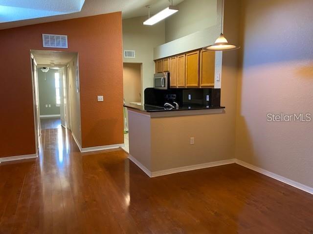 A kitchen with wood cabinets and a breakfast bar overlooks a room with hardwood floors — 5005 CITY STREET UNIT 1335, ORLANDO, FL
