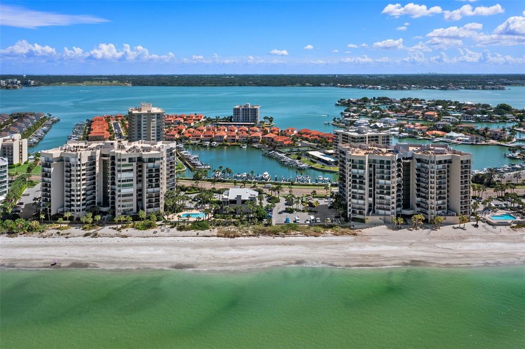 An aerial view shows two large beachfront condominium buildings flanking a marina and residential area — 1660 GULF BOULEVARD UNIT 706, CLEARWATER BEACH, FL