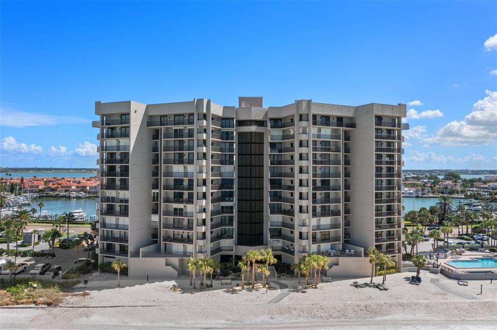 An aerial view of a multi-story beige condominium building situated on a sandy beach — 1660 GULF BOULEVARD UNIT 706, CLEARWATER BEACH, FL