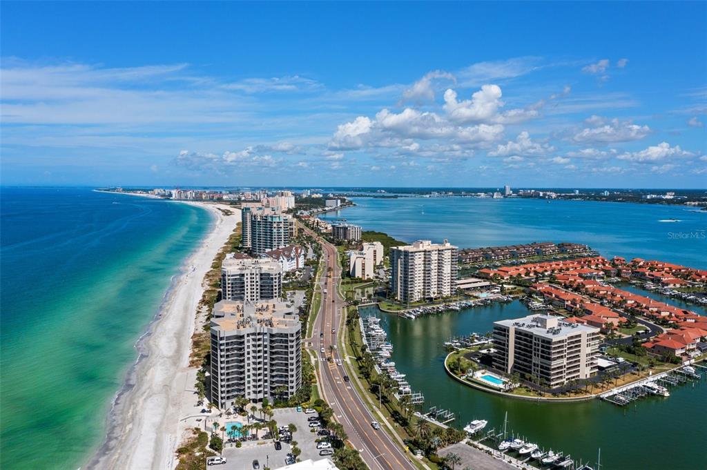 An aerial view shows a coastal road separating a sandy beach from a marina — 1660 GULF BOULEVARD UNIT 706, CLEARWATER BEACH, FL