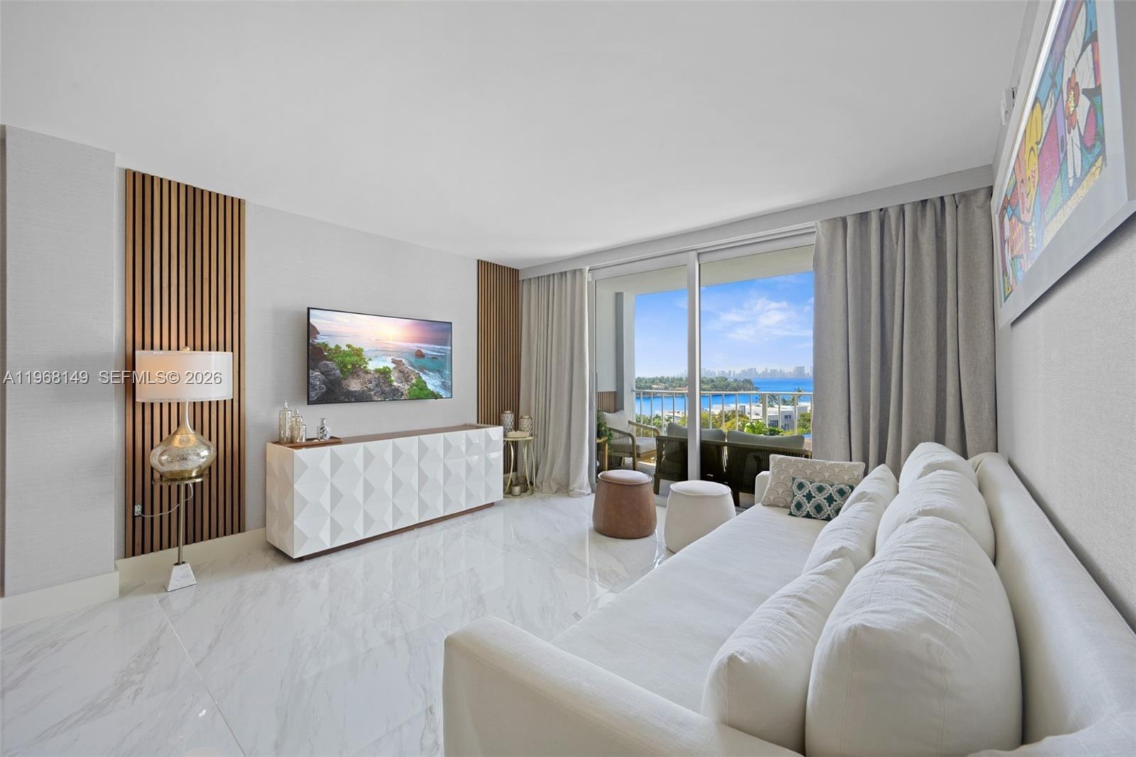 A living room features a white sofa, a geometric media console, and a balcony view — 6900 Bay Dr # 8A, Miami Beach FL 33141, MIAMI BEACH, FL