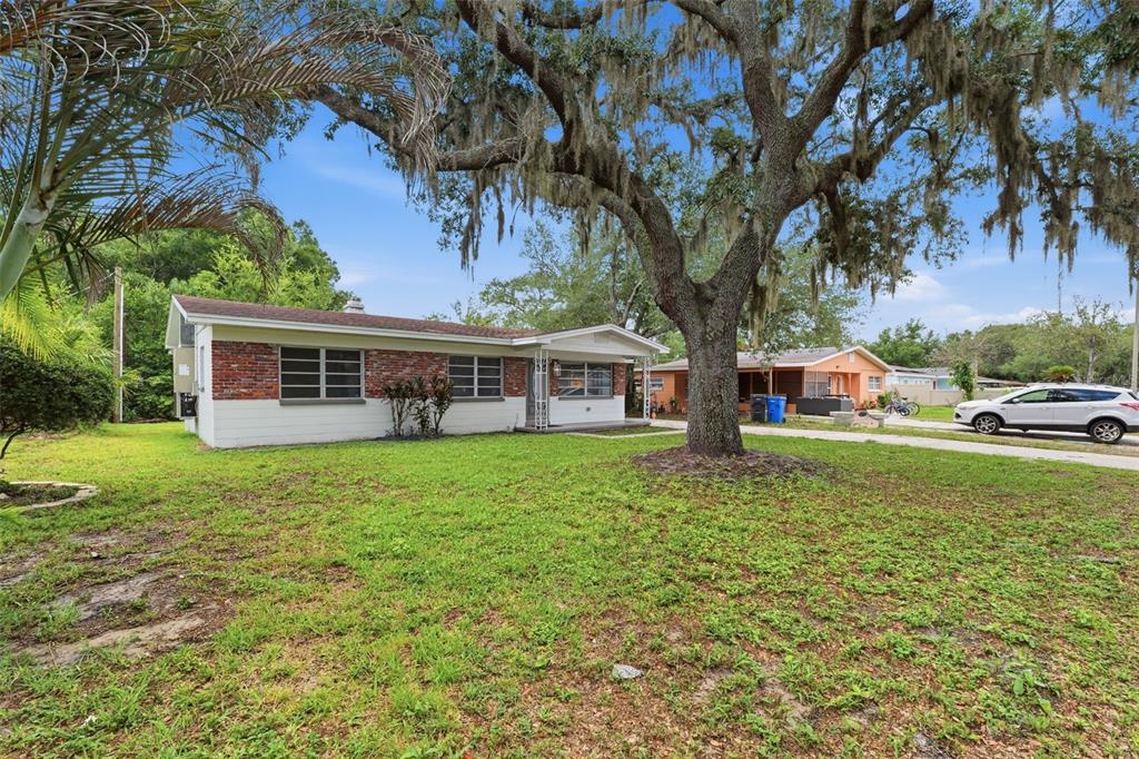 A covered concrete porch runs along the side of a house with white brick walls — 7815 PINE HILL DRIVE, TAMPA, FL