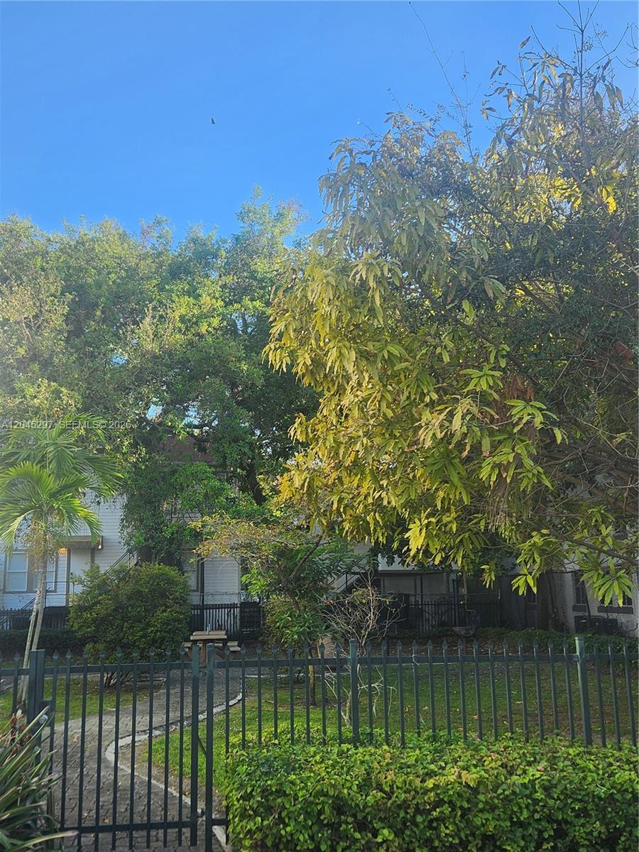 A view of a house exterior partially obscured by trees behind a black metal fence — 412 NW 4th St, Miami FL 33130, MIAMI, FL