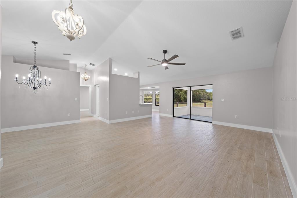 A spacious living room features light wood-look tile flooring, vaulted ceilings, and two decorative chandeliers — 4170 HICKORY TREE ROAD, ST CLOUD, FL