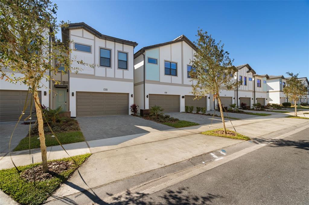 A row of modern townhouses with attached garages and paved driveways under a clear sky — 10454 EBB TIDE LANE, ORLANDO, FL
