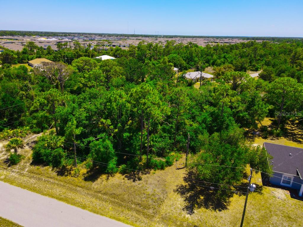 An aerial view shows a wooded vacant lot next to a house and paved road — 15531 FACTORY AVENUE, PORT CHARLOTTE, FL