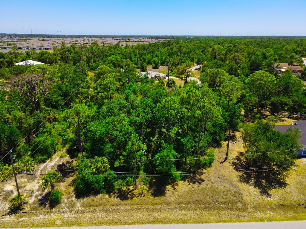 An aerial view shows a wooded, undeveloped lot bordered by a road and nearby houses — 15531 FACTORY AVENUE, PORT CHARLOTTE, FL