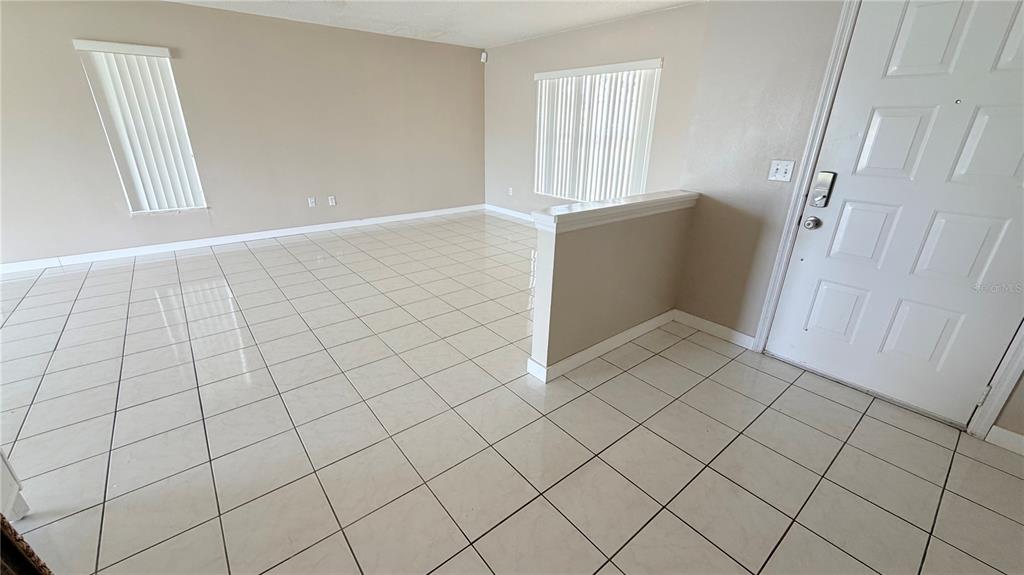 An empty room with light-colored tile flooring, beige walls, and a white front door — 3113 FAIRFIELD DRIVE, KISSIMMEE, FL