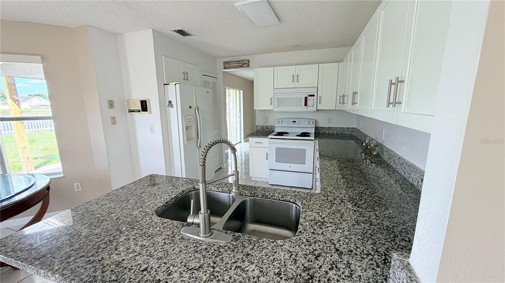 A kitchen features white cabinets, granite countertops, a double sink, and white appliances — 3113 FAIRFIELD DRIVE, KISSIMMEE, FL