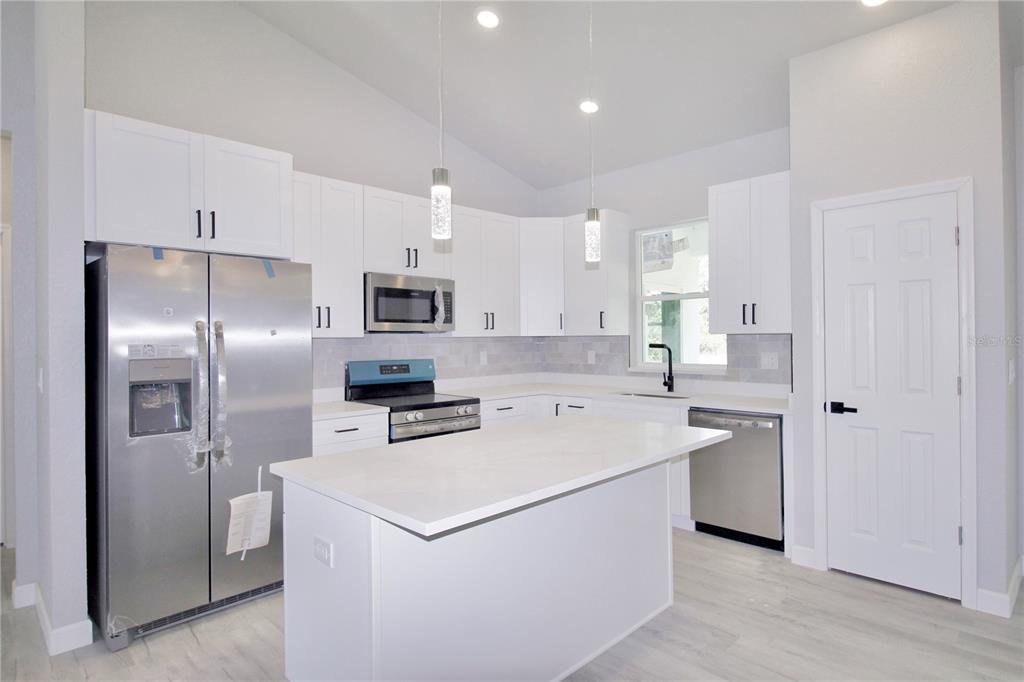 A modern kitchen features white cabinets, stainless steel appliances, a center island, and light flooring — 4000 GARIENDA AVENUE, SEBRING, FL