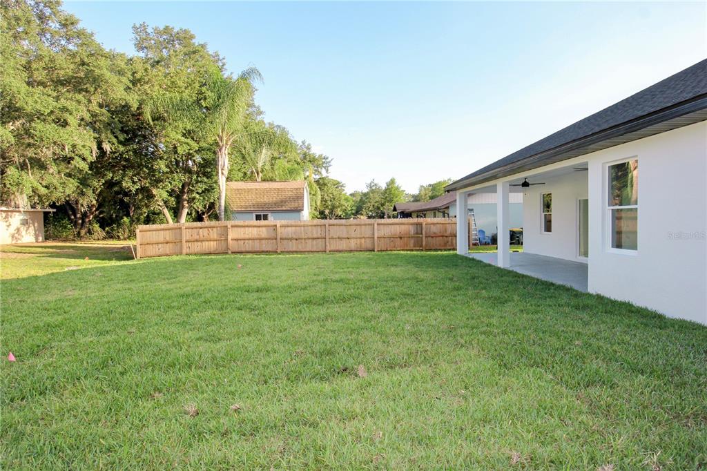 A grassy backyard features a wooden fence, a covered patio, and mature trees — 4000 GARIENDA AVENUE, SEBRING, FL