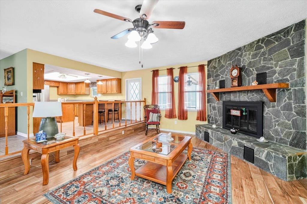 A living room with a stone fireplace, wood floors, and an elevated kitchen area — 6483 SE 88TH STREET, OCALA, FL