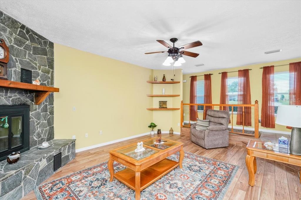 A living room features a stone fireplace, wood flooring, built-in corner shelves, and a ceiling fan — 6483 SE 88TH STREET, OCALA, FL