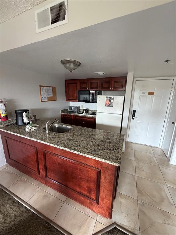 A kitchen features a granite-topped island, dark wood cabinets, and tile flooring — 6336 PARC CORNICHE DRIVE UNIT 3307, ORLANDO, FL