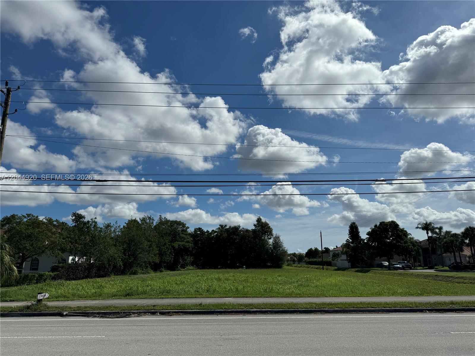 A vacant, grassy lot sits beside a road under a bright, cloudy blue sky — 3494 S Jog Rd, Green Acres FL 33467, GREEN ACRES, FL