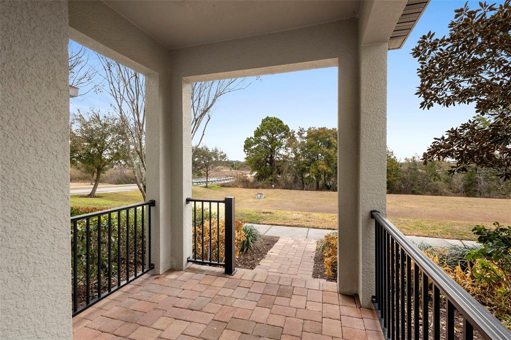 A covered brick porch with black metal railings overlooks a grassy yard and distant trees — 14989 APOLLO BOND DRIVE, WINTER GARDEN, FL