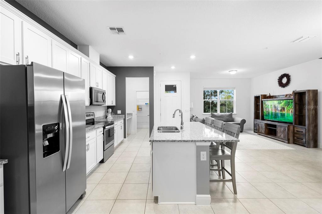 A modern kitchen with white cabinets and granite countertops opens into a living room area — 14989 APOLLO BOND DRIVE, WINTER GARDEN, FL