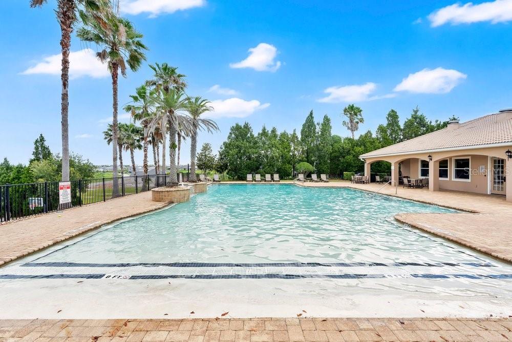 A swimming pool with a brick deck and palm trees sits beside a building exterior — 4265 JULIANA LAKE DRIVE, AUBURNDALE, FL