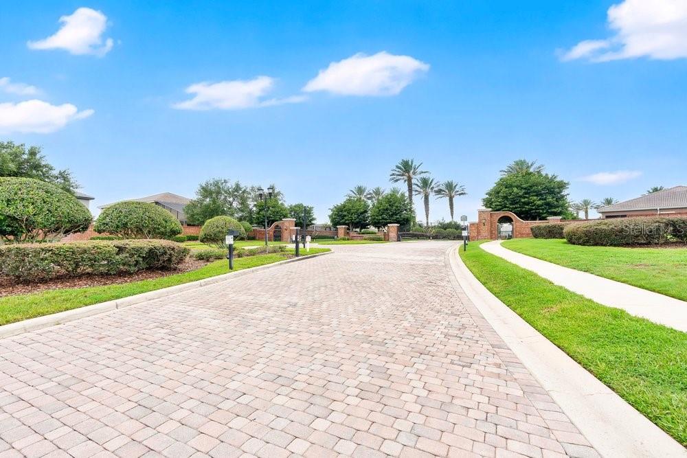 A paved driveway leads toward a gated entrance with brick pillars and palm trees — 4265 JULIANA LAKE DRIVE, AUBURNDALE, FL