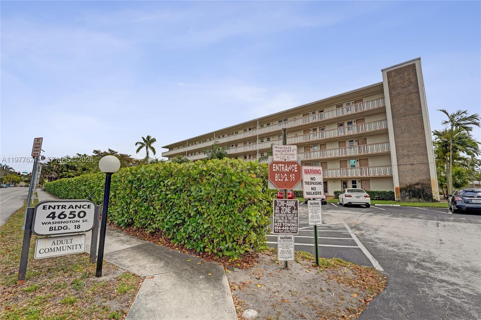 A multi-story apartment building stands behind a hedge with various parking and entrance signs — 4650 Washington St # 209, Hollywood FL 33021, HOLLYWOOD, FL