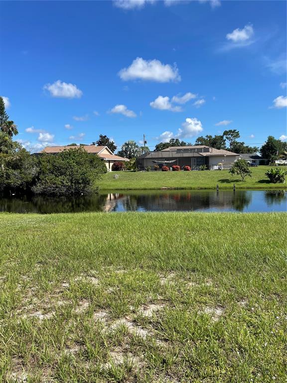 A view of a grassy yard overlooking a pond with houses in the background — 130 MARK TWAIN LANE, ROTONDA WEST, FL