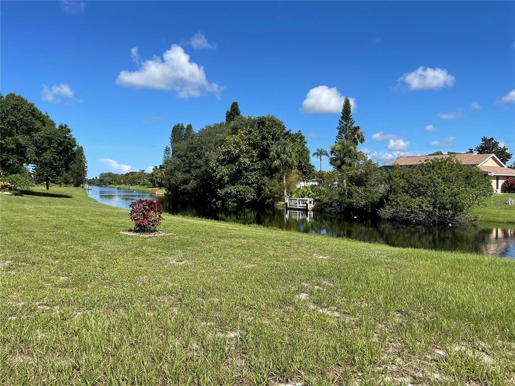 A grassy lawn slopes down to a canal bordered by trees and a small dock — 130 MARK TWAIN LANE, ROTONDA WEST, FL