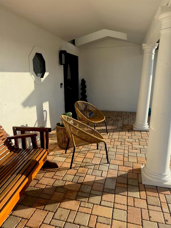 A covered patio features a paver floor, two wicker chairs, and a wooden bench — 452 BATH CLUB BOULEVARD N, NORTH REDINGTON BEACH, FL