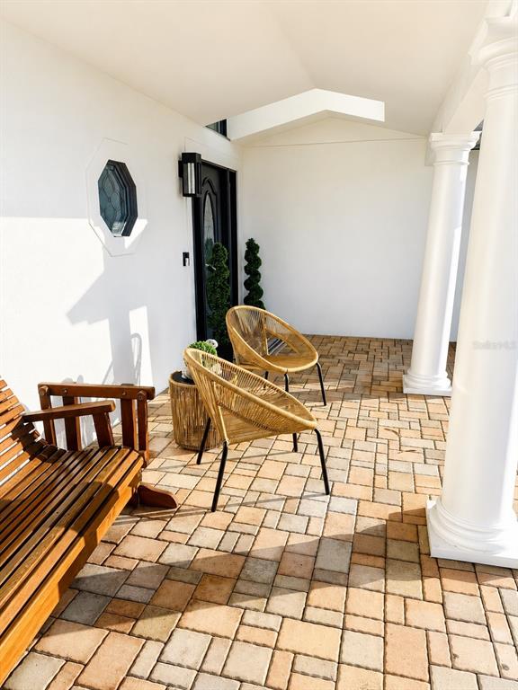 A covered patio features a wooden bench, two wicker chairs, and a stone paver floor — 452 BATH CLUB BOULEVARD N, NORTH REDINGTON BEACH, FL