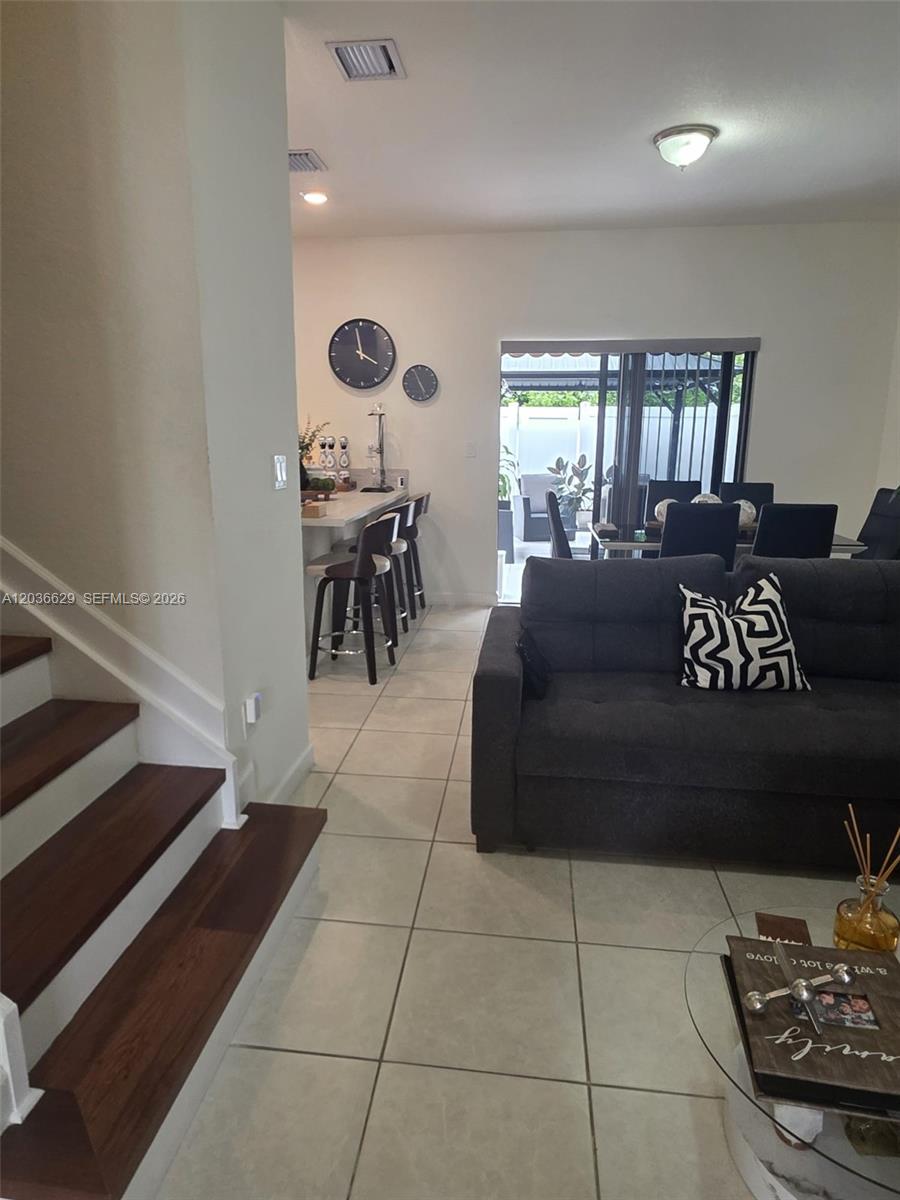 A living room with a staircase, tile flooring, a dark sofa, and a kitchen bar — 10963 W 32nd Ln, Hialeah FL 33018, HIALEAH, FL
