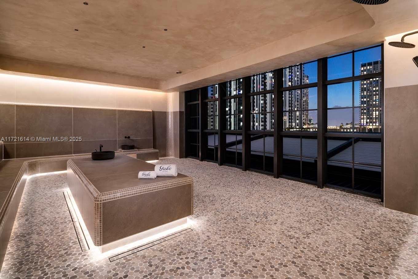 This spa room features a central stone massage table, pebble flooring, and floor-to-ceiling windows — 159 NE 6 # 3912, Miami FL 33132, MIAMI, FL