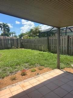 A view of a backyard with a grassy lawn, wooden fence, and a covered patio — 18970 Cloud Lake Circle, Boca Raton FL 33496, BOCA RATON, FL