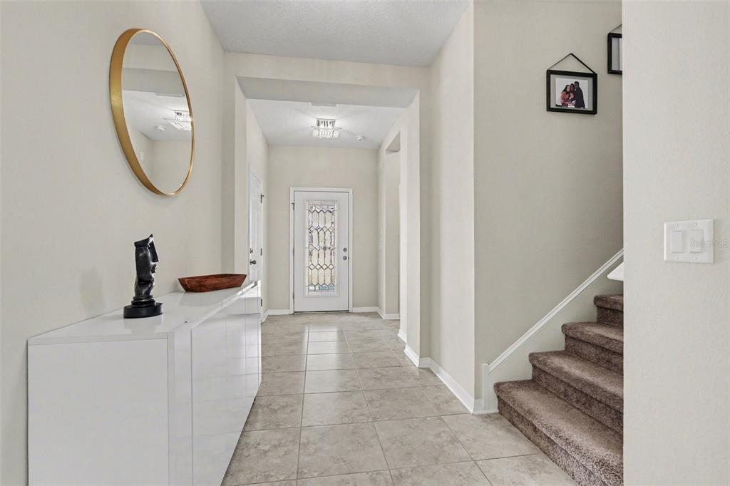 A bright entryway features tiled flooring, a white console table, a round mirror, and stairs — 30789 PARROT REEF COURT, WESLEY CHAPEL, FL